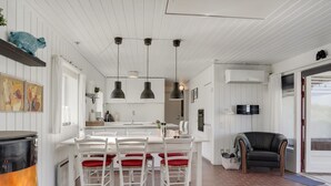 A modern kitchen with white cabinetry, a dining area with red cushioned chairs, and a black leather sofa. - "Marjon" - 400m from the sea by Interhome (Pandrup)