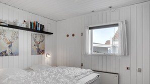 A bedroom with a bed, a window, a radiator, and a shelf with books and a decorative item. - "Marjon" - 400m from the sea by Interhome (Pandrup)
