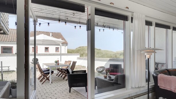 A covered outdoor area with a table and chairs, a wicker chair, a sofa, and a window with curtains. - "Marjon" - 400m from the sea by Interhome (Pandrup)