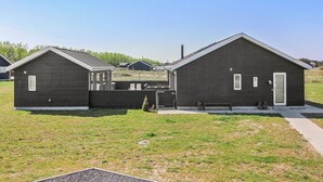 Deux cabanes de couleur sombre, séparées par un petit espace patio, et entourées d’un champ d’herbe.