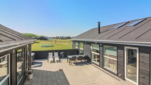 Un bâtiment moderne doté d’un patio, de grandes fenêtres et offrant une vue sur un champ verdoyant.