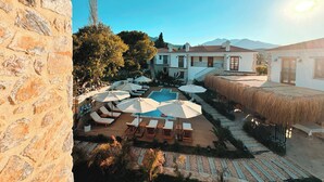 A poolside area with lounge chairs and umbrellas, a stone wall, and a building with a white facade and red roof. - Dilek Hanım Konağı Datça (Datça)