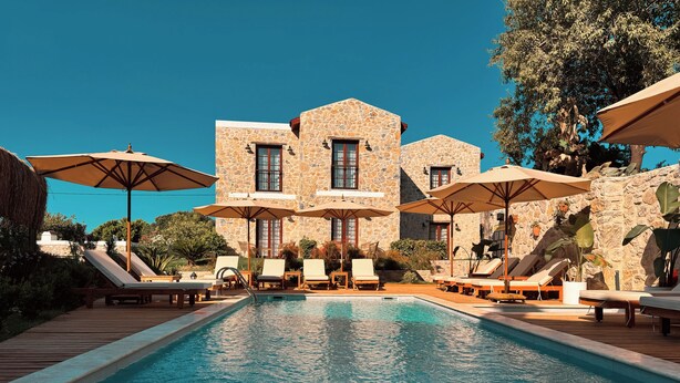 A pool area with lounge chairs and umbrellas, a stone building in the background, and a clear blue sky. - Dilek Hanım Konağı Datça (Datça)