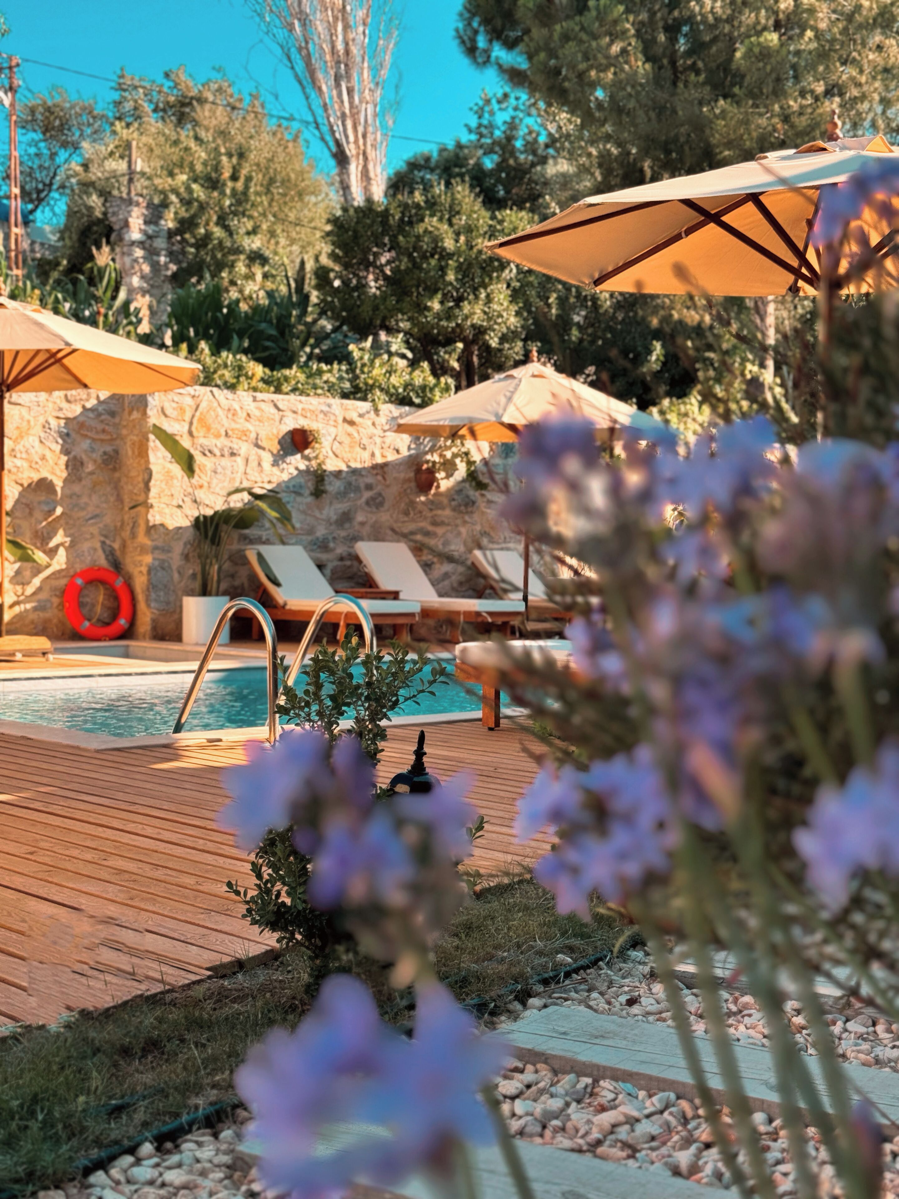 Un área de piscina con sillas de descanso, sombrillas y una pared de piedra.