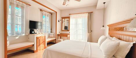 A bedroom with a large bed, a wooden headboard, a ceiling fan, a desk with a chair, a TV, and a window with curtains.