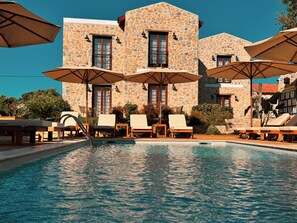 A stone building with a pool, lounge chairs, and umbrellas.