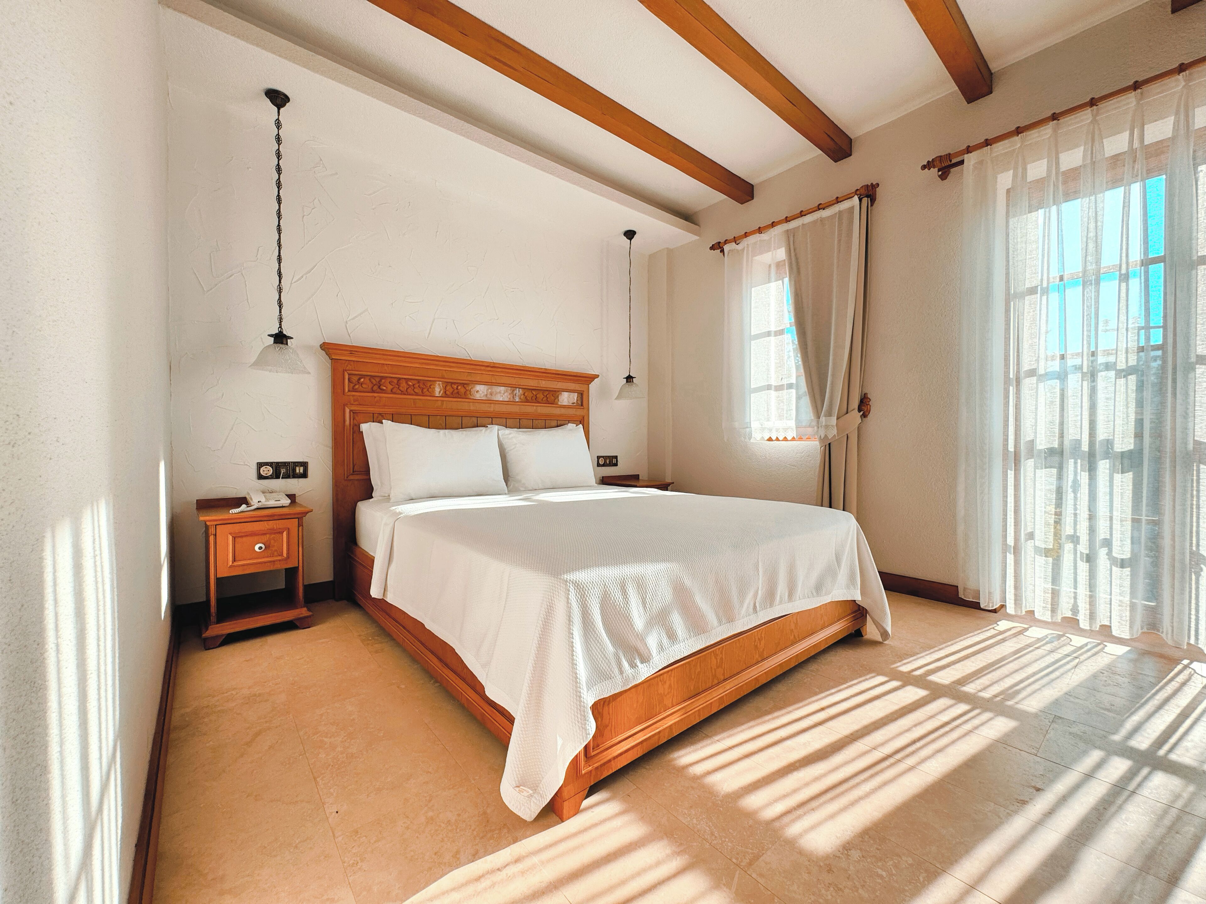 A bedroom with a wooden bed, a nightstand, a lamp, and a window with curtains.
