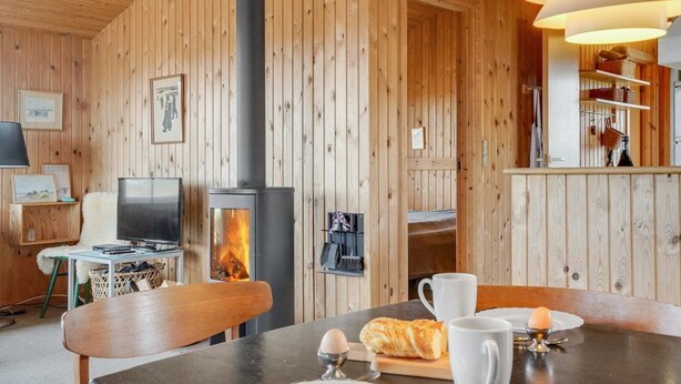 Een gezellige kamer met houten inrichting, een open haard, een eettafel gedekt met borden, een croissant en een mok.