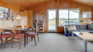 Een houten interieur met een eethoek, een bank en uitzicht door een glazen deur.