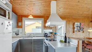 Een compacte keuken met houten lambrisering, een centraal kookeiland en uitzicht op een huis door het raam.