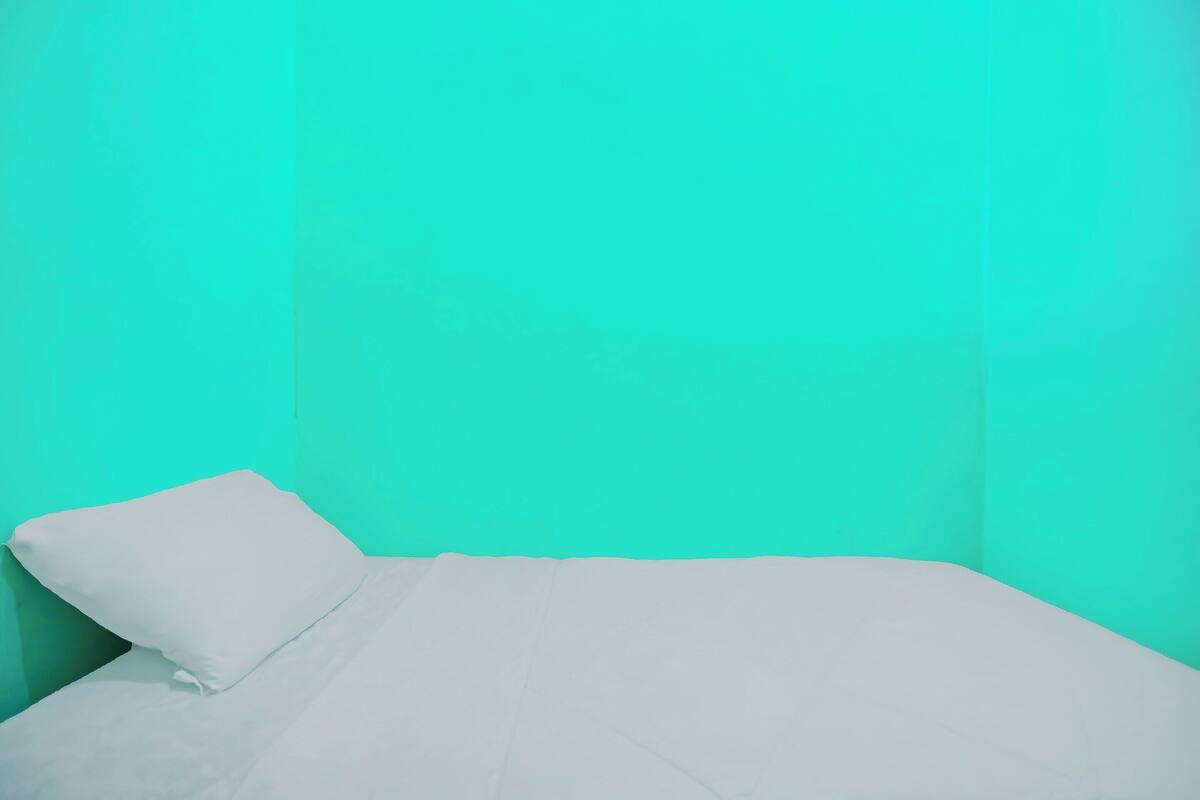Una cama individual con colchón y almohada blancos en una habitación con paredes turquesa.