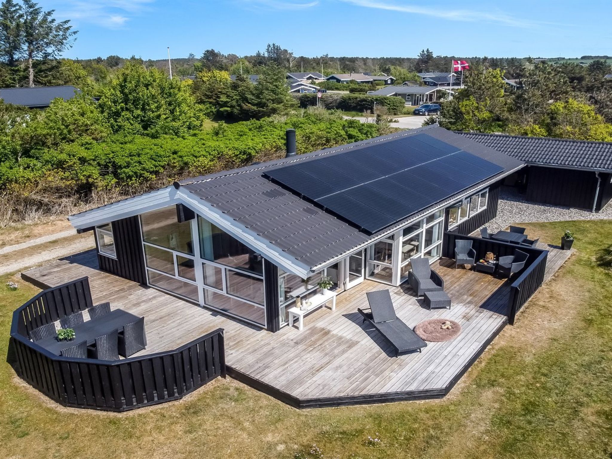 A modern house with a large deck, solar panels, and a glass-enclosed patio area.