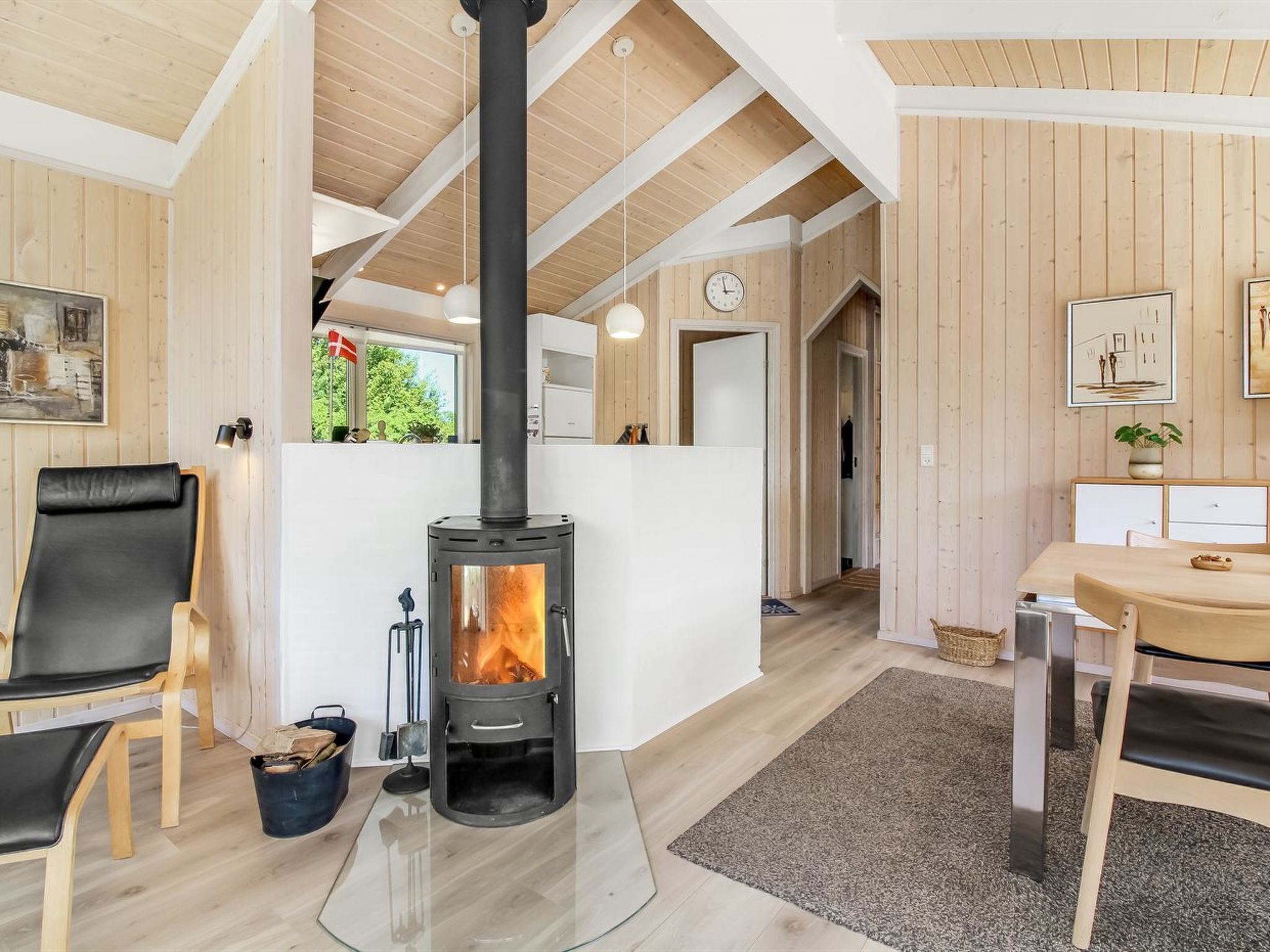 A cozy room with a central wood-burning stove, wooden walls, a dining area with a table and chairs, and a comfortable seating area with a chair.