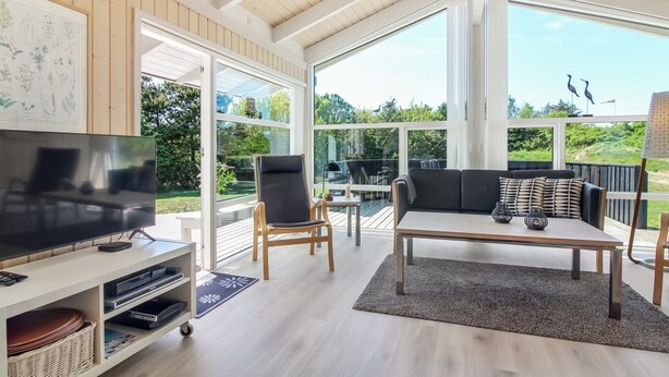 A spacious living area with a TV, seating, and large windows offering a view of the outdoors.