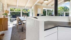 A modern kitchen with a large island, wooden ceiling, and large windows.