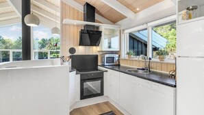 A modern kitchen with a black stove, white cabinets, and a large window overlooking greenery.