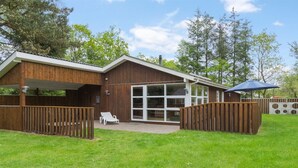 A wooden house with a covered patio, a glass door, and a fenced yard.