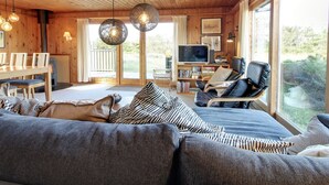 Un interior de cabaña acogedor con techo de madera, un sofá, un televisor y una zona de comedor.