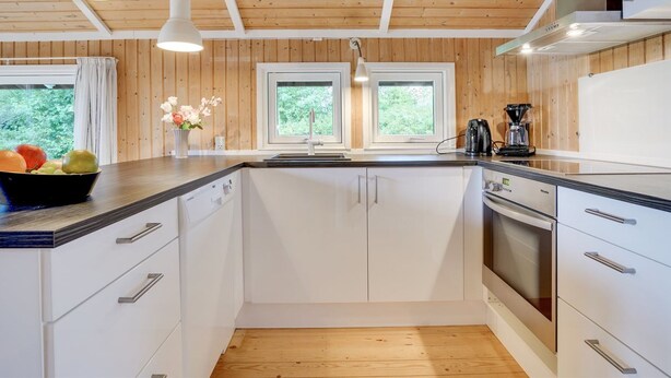 A modern kitchen with wooden paneling, white cabinets, a black countertop, and a built-in oven. - "Nafni" - 200m from the sea by Interhome (Væggerløse)