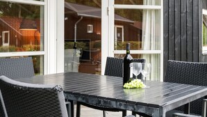 A covered patio area with a table set for two, featuring a bottle of wine and a bowl of grapes. - "Nafni" - 200m from the sea by Interhome (Væggerløse)