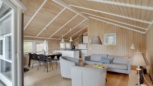 A spacious living area with a high ceiling, wooden walls, a sofa, a dining table with chairs, and a kitchen area. - "Nafni" - 200m from the sea by Interhome (Væggerløse)