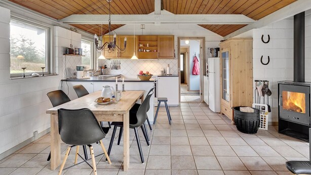 A modern kitchen with wooden beams, a dining area with chairs, a central island, and a wood-burning stove. - "Raika" - 450m to the fjord by Interhome (Tarm)