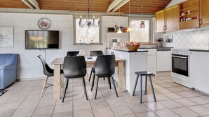 A modern kitchen with white cabinets, a dining area with black chairs, a wooden ceiling, and a TV mounted on the wall. - "Raika" - 450m to the fjord by Interhome (Tarm)