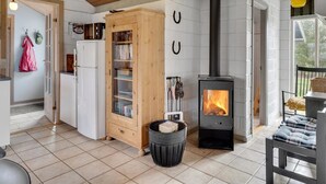 A cozy interior with a wood-burning stove, a white refrigerator, a wooden cabinet with glass doors, and a tiled floor. - "Raika" - 450m to the fjord by Interhome (Tarm)