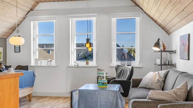 A cozy loft-style room with a sloped ceiling, large windows, a dining area, and a seating area with a sofa and a table.