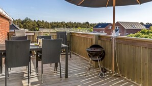 A wooden deck with a table and chairs, a barbecue grill, and a large umbrella.