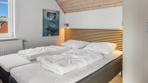 A bedroom with a sloped ceiling, a bed with white bedding, a radiator, and a poster on the wall.