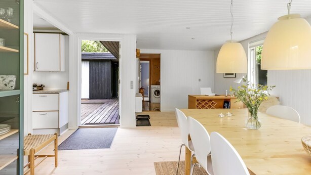 A modern kitchen with white cabinets, a wooden dining table, and a view to a backyard. - "Malti" - 300m from the sea by Interhome (Sæby)