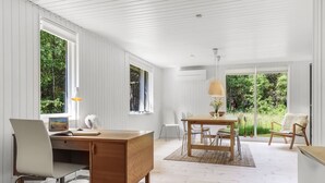 A modern room with a wooden desk, chairs, a dining table, and a large window offering a view of greenery. - "Malti" - 300m from the sea by Interhome (Sæby)