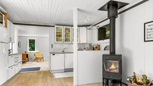 A modern kitchen with a wood-burning stove, white cabinetry, and a dining area with a yellow chair. - "Malti" - 300m from the sea by Interhome (Sæby)