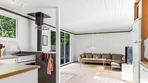 A modern kitchen with a stove, hanging utensils, and a dining area with a sofa and table. - "Malti" - 300m from the sea by Interhome (Sæby)