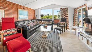A cozy living room with a black leather sofa, red armchairs, and a patterned rug.