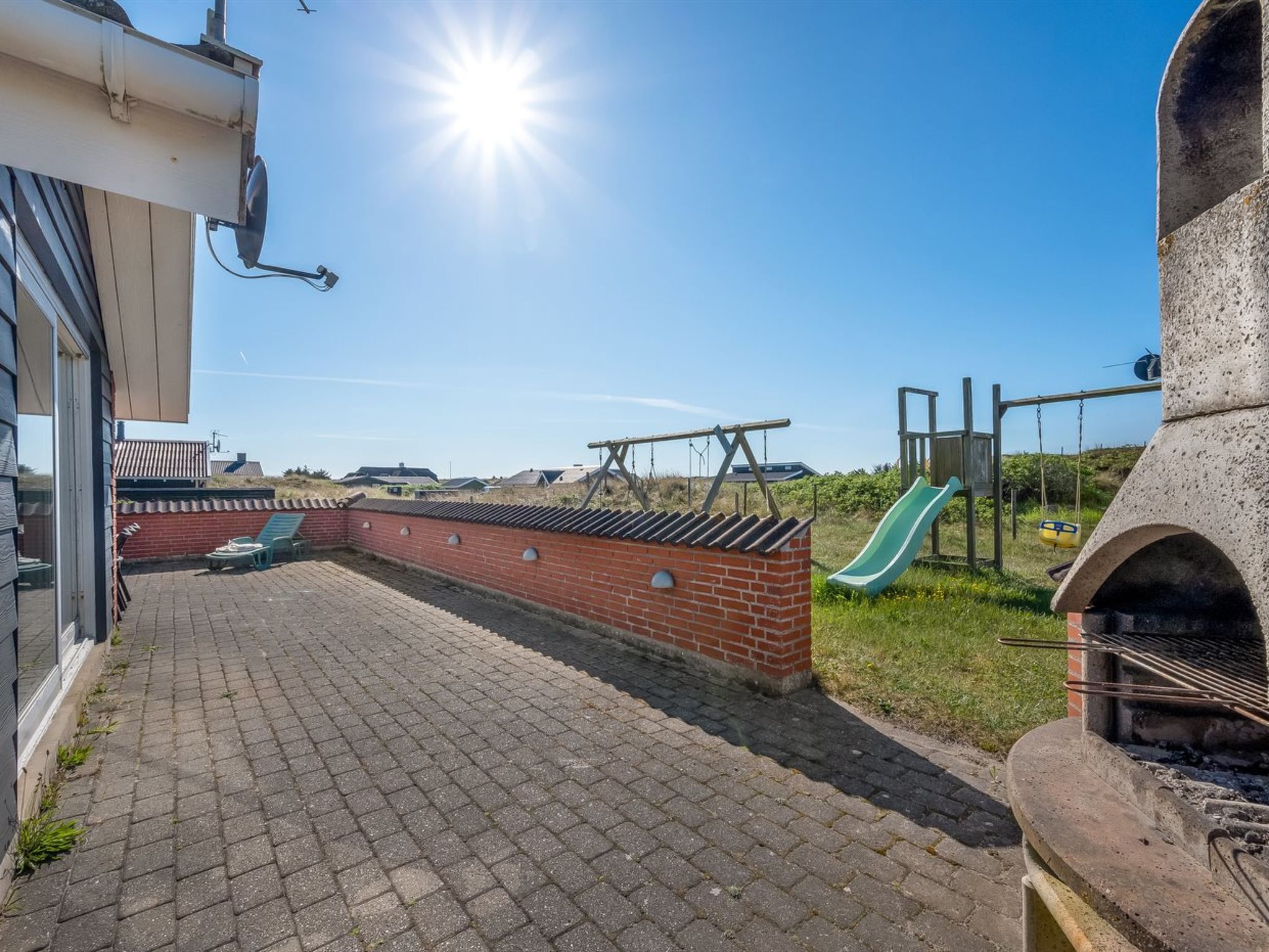 Une terrasse avec un sol en briques, un mur en briques, un toboggan vert et un espace barbecue.