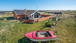 A house with solar panels, a small boat, and a swing set in a grassy area.