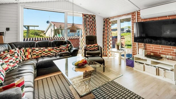 A modern living room with a leather sofa, a glass coffee table, and a TV mounted on a brick wall.