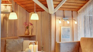 Une pièce chaleureuse avec des murs et un plafond en bois, un canapé, une table avec des bougies et des lampes suspendues.