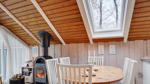 Une pièce chaleureuse avec une table ronde en bois, des chaises blanches, un poêle à bois et une lucarne.