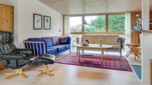 Ein modernes Wohnzimmer mit einem schwarzen Ledersessel, einem blauen Sofa, einem Holztisch und einem roten Teppich mit Muster.