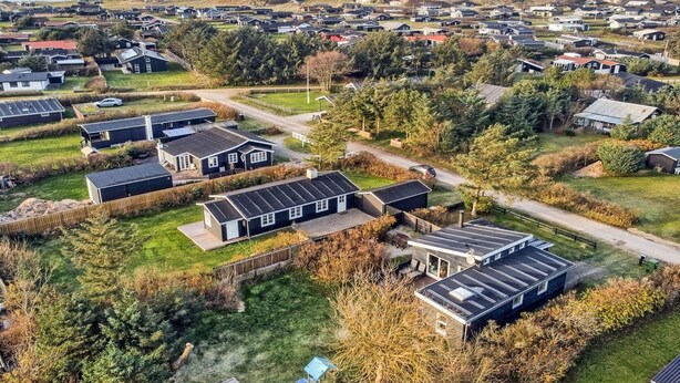 Eine Vogelperspektive zeigt eine Wohngegend mit mehreren Häusern, von denen einige mit Solaranlagen ausgestattet sind, umgeben von viel Grün und einem Blick auf das Meer in der Ferne.
