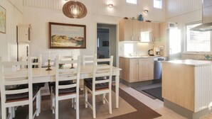 Eine moderne Küche mit Holzausstattung, einer zentralen Kochinsel und einem Essbereich mit weißen Stühlen und einem Tisch.