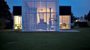 Une maison moderne en verre, dont l’intérieur est visible et qui comprend un espace repas et un escalier.