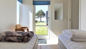 Une chambre avec deux lits, une chaise et une porte donnant sur un balcon d’où l’on peut admirer un arbre et un immeuble.
