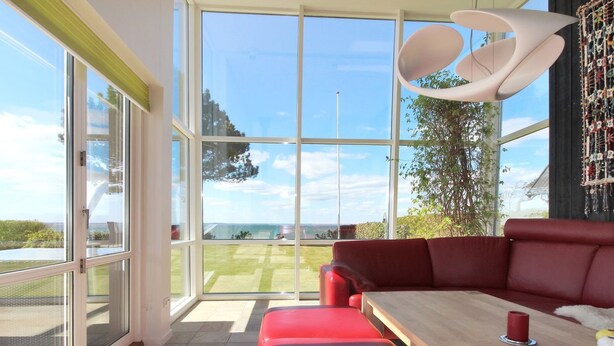 Un salon moderne avec un canapé rouge, une table basse en bois et une grande fenêtre donnant sur un paysage verdoyant.