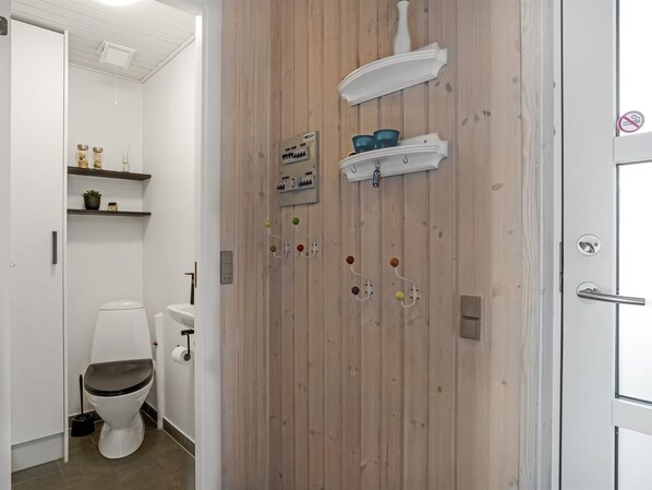 A bathroom with a wooden wall, a toilet, a sink, and shelves with toiletries.
