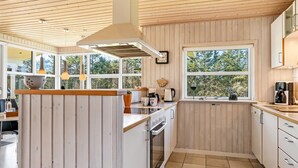 Une cuisine moderne avec un lambris en bois, un îlot central et de grandes fenêtres donnant sur un paysage verdoyant.