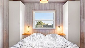 Une chambre avec un grand lit, des murs en bois, une fenêtre et deux lampes de chevet.